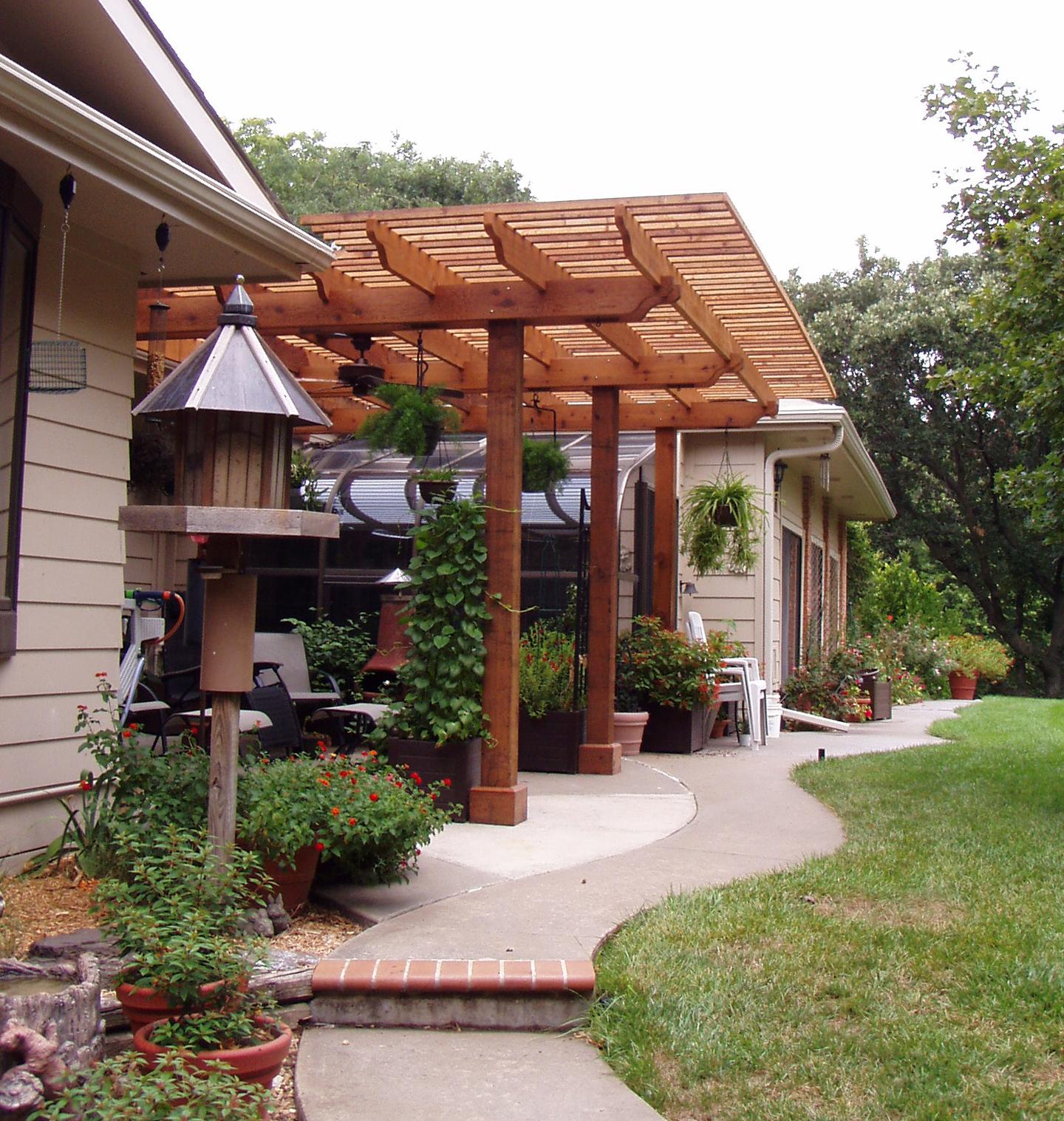 Backyard patio with wooden pergola, potted plants, and garden seating.